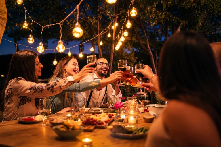Un grupo de amigos brinda durante una cena al aire libre bajo luces cálidas